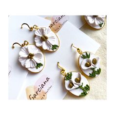 three earrings with white flowers on them sitting next to a piece of paper and a note