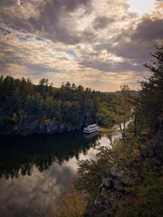 a boat traveling down a river surrounded by forest under a cloudy sky with sun peeking through the clouds