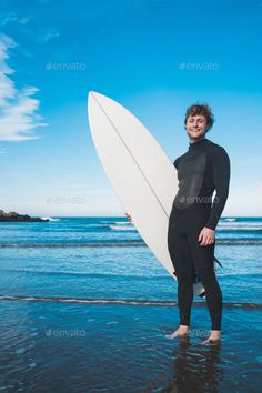 a man in a wet suit holding a surfboard on the beach - stock photo - images