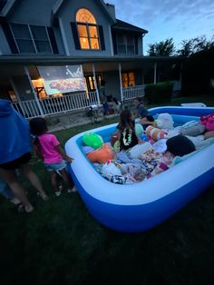 children playing in an inflatable pool on the lawn at night with adults watching