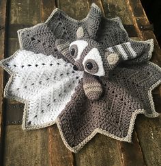 a crocheted raccoon is laying on top of a wooden table with a white and gray blanket