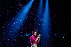 a man standing on top of a stage holding a microphone in front of blue lights