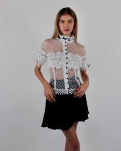 Introducing the elegant Alicia Blouse, crafted from Swiss Point D’Esprit with cotton lace ruffles, Venise trims, and satin baby bows. This soft, fitted blouse features an empire focus, adorned with delicate ruffles at the neckline and sleeves, complemented by satin pearl buttons at the center front. Available in White and Black or Black on Black. Swiss Point D’Esprit Cotton lace ruffles with Venise trims Satin pearl buttons Dry clean only Each piece is made to order and handcrafted in our atelie Chic Short Sleeve Blouse With Lace Patchwork, White Fitted Lace Top With Contrast Lace, Fitted White Lace Top With Contrast Lace, Short Sleeve Lace Top For Spring Formal, Elegant Short Sleeve Lace Top For Spring, Formal Short Sleeve Lace Top For Spring, Short Sleeve Lace Top With Ruffles, Elegant Spring Lace Top With Contrast Lace, Elegant Summer Lace Top With Lace Cuffs