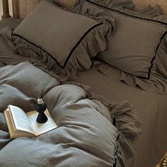 an open book is sitting on top of a bed with ruffled sheets and pillows