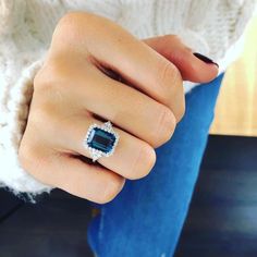 a woman's hand wearing a ring with an emerald stone in the middle and diamonds on it