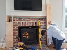 a man working on a brick fireplace with a tv above it