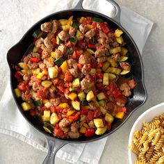 a skillet filled with meat and veggies next to pasta