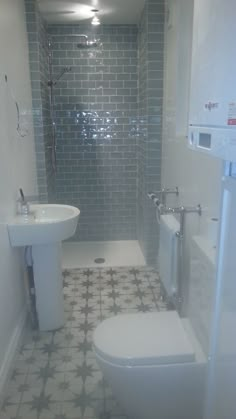 a white toilet sitting next to a sink in a bathroom under a shower stall with grey tiles on the walls