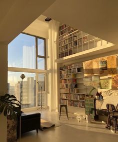 a living room filled with lots of books and furniture next to a large open window