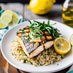 a white plate topped with fish and rice next to lemons on a wooden table