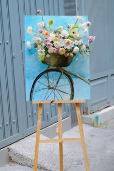 an easel is holding a painting with flowers in the basket on it's wheels