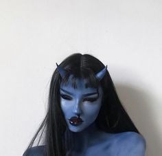 a woman with blue paint on her face and long black hair, wearing devil makeup