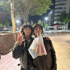 two people standing next to each other with bags on their shoulders and one holding up the peace sign