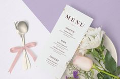 a plate with flowers and a menu on it next to a knife, fork and spoon