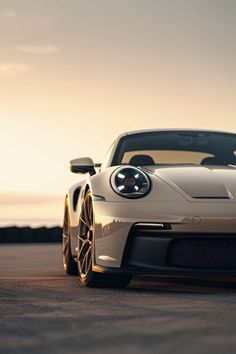 a white sports car parked on top of a parking lot next to the ocean at sunset