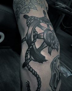 a man's arm with an anchor, steering wheel and rope tattoo on it