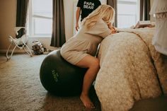 a pregnant woman is sitting on an exercise ball in her bedroom while a man stands nearby