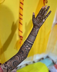 a woman's hand with henna on it and yellow wall in the background