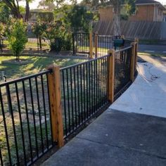 a black iron fence next to a sidewalk in a residential area with grass and trees