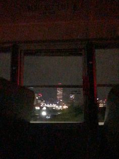 the view from inside a bus at night with city lights visible in the distance and buildings lit up behind it