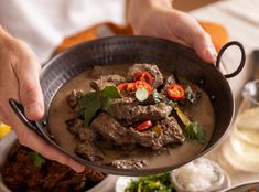 a person holding a bowl filled with meat and veggies on top of a table