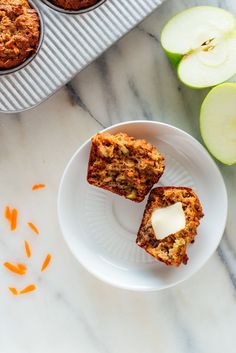 two muffins on a white plate with apples and carrots next to them