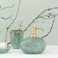 a green soap dispenser sitting on top of a counter next to a cup