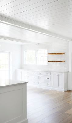 an empty kitchen with white cabinets and wood floors