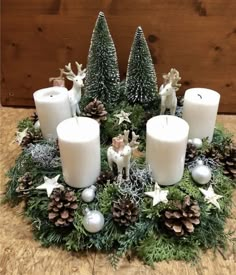 some white candles are sitting in a wreath with pine cones and other decorations on it