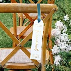 a wooden chair with a tag hanging from it's back in front of some flowers