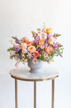 a vase filled with lots of flowers on top of a marble topped table next to a white wall