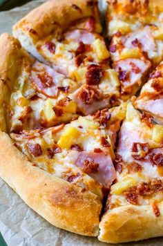 a pizza with ham and pineapple on it sitting on top of a piece of wax paper