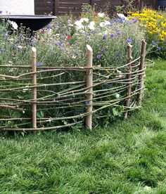 a fence made out of branches and sticks in the grass with flowers growing behind it