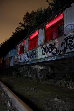 an abandoned train car with graffiti on the side and red light coming from it's windows