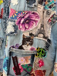 a cat is sitting in the pocket of a jean jacket with patches and flowers on it