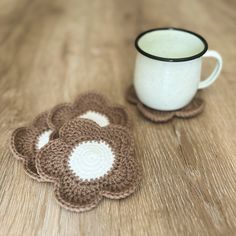 four crocheted coasters sitting on top of a wooden table next to a coffee cup