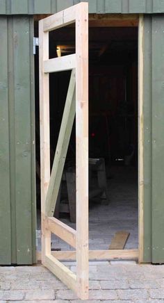 an open wooden door in front of a green building with brick flooring and walls