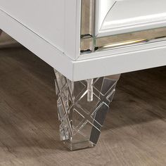 a clear glass vase sitting on top of a wooden floor next to a white dresser