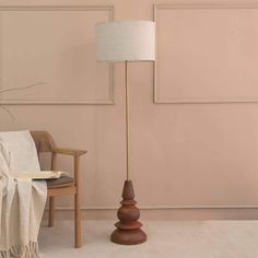 a wooden floor lamp next to a chair in a room with pink walls and white carpet