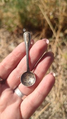 a hand holding a small spoon in it's right hand with grass and weeds behind it