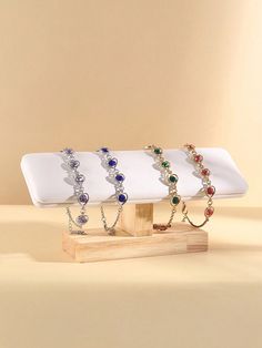 three bracelets are on display in front of a beige background and one has a wooden stand