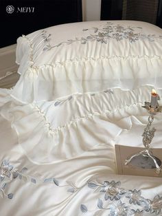 a white bed topped with pillows and a pillow case next to a candle on top of it