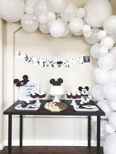 a table topped with cupcakes and cake next to white balloons in the shape of mickey mouse