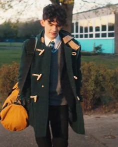 a young man is walking down the street wearing a green coat and black pants, holding a yellow handbag