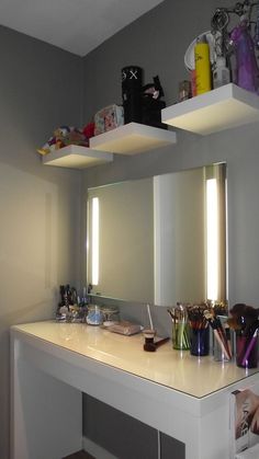 a white counter top sitting under a mirror next to a shelf filled with makeup and other items