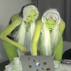 two women dressed in green are looking at a laptop