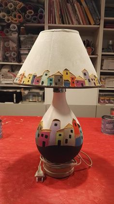 a lamp that is sitting on top of a red tablecloth with houses painted on it