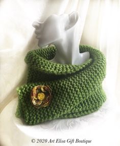 a green knitted scarf with a button on the end and a white vase in the middle