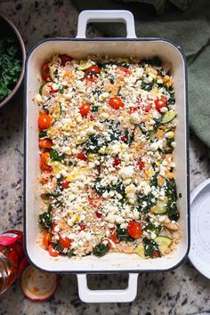 a casserole dish with tomatoes, spinach and feta cheese on top