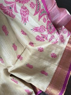 This is an elegant handloom tussar silk saree mixed with subtle tissue. Body is natural tussar colour/ivory shade with magenta colour border. Borders are woven with beautiful zari motifs. Body and pallu have beautiful jamdani motifs in magenta colour. Pallu has beautiful magenta and gold zari stripes and it is finished with tassels.  Saree comes with an unstitched blouse piece with zari borders. *Colour may vary slightly depending upon the lighting  *Fall and pico are done *All sales are final  *Dry clean only Luxury Tussar Silk Saree With Tilla Details, Pink Tussar Silk Dupatta With Weaving Work, Traditional Saree With Printed Border In Mulmul, Pink Raw Silk Saree With Weaving Work, Tussar Silk Dupatta With Woven Motifs, Luxury Tussar Silk Saree With Zari Weaving, Handloom Tussar Silk Dupatta, Pink Art Silk Saree With Woven Motifs, Traditional Mulmul Saree With Printed Border